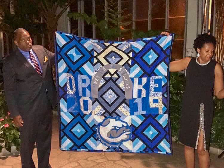 man and woman holding up blue greek symbol quilt