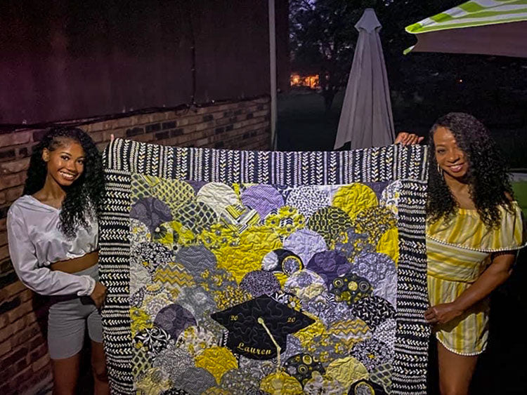 two women holding up multicolored graduation quilt