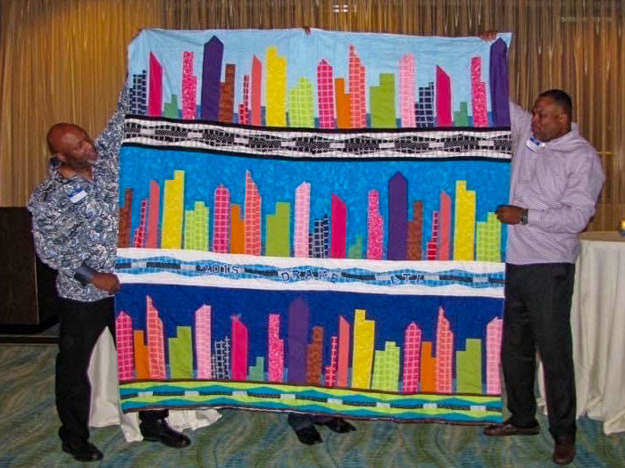 two men holding up multicolored skyline quilt